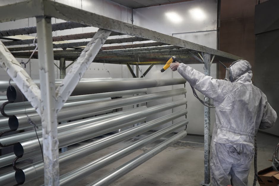 Technician applying powder coating to metal pipes in a workshop setting.
